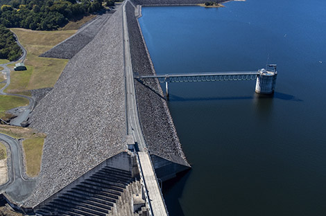 Drone view of large scale Australian concrete dam wall and spillway with overhead pedestrian and traffic bridge