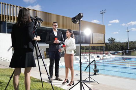 A man and woman holding microphones with a woman holding a video camera