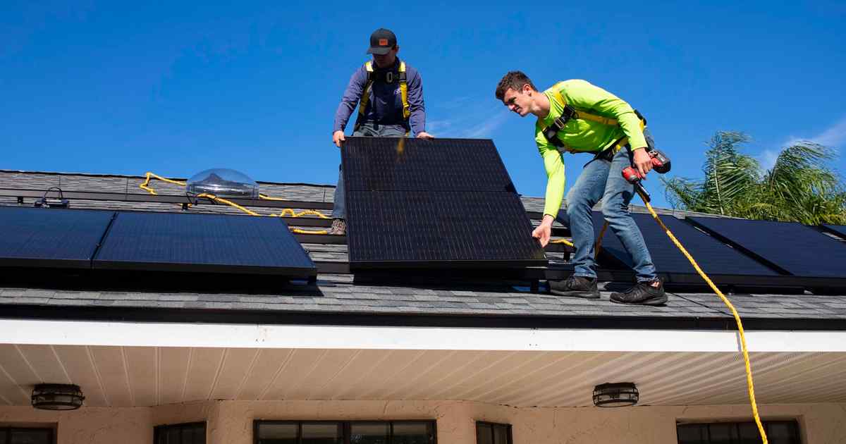 Two men on the roof of a house installing solar pannels.