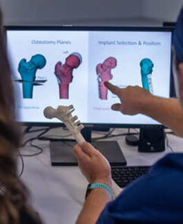 Person holding a hip model while discussing surgical options displayed on a screen.