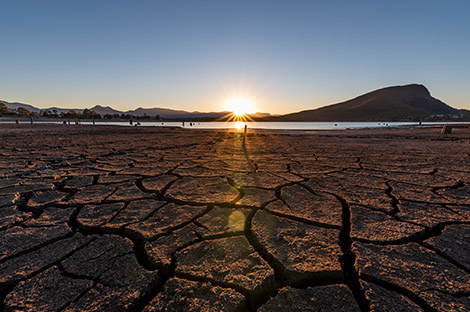 The sun setting over a lake showing the dry cracks in lake bed on a clear and sunny day