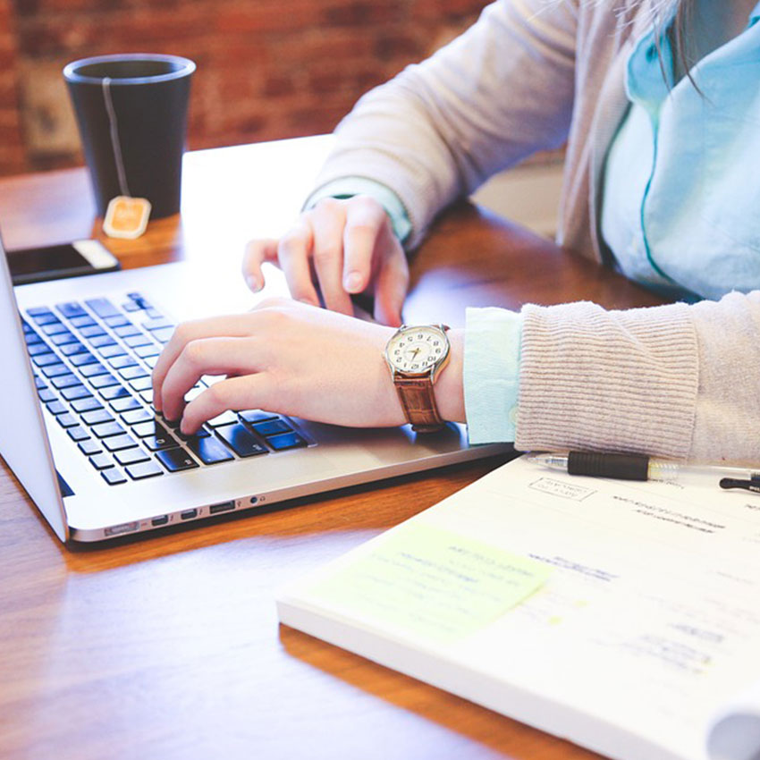 a person types on a laptop with a notepad beside them