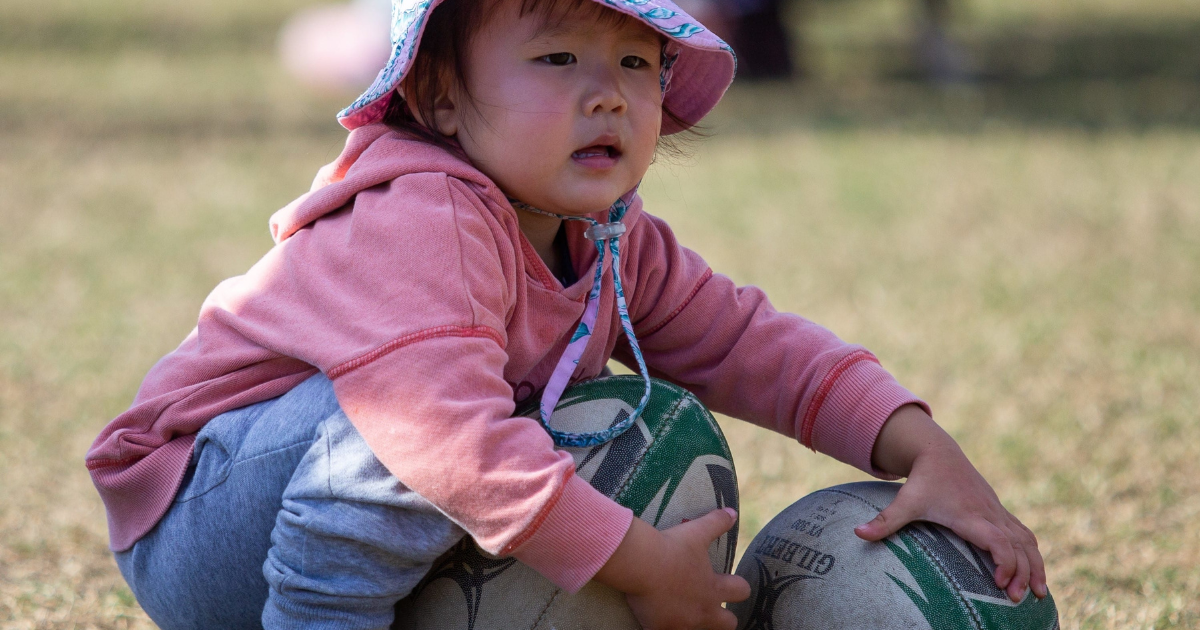 A child holding two rugby balls.