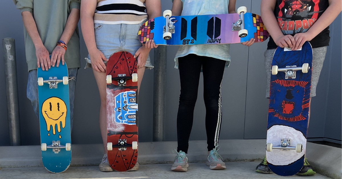 Seven children holding their painted skateboards with different designs on them.