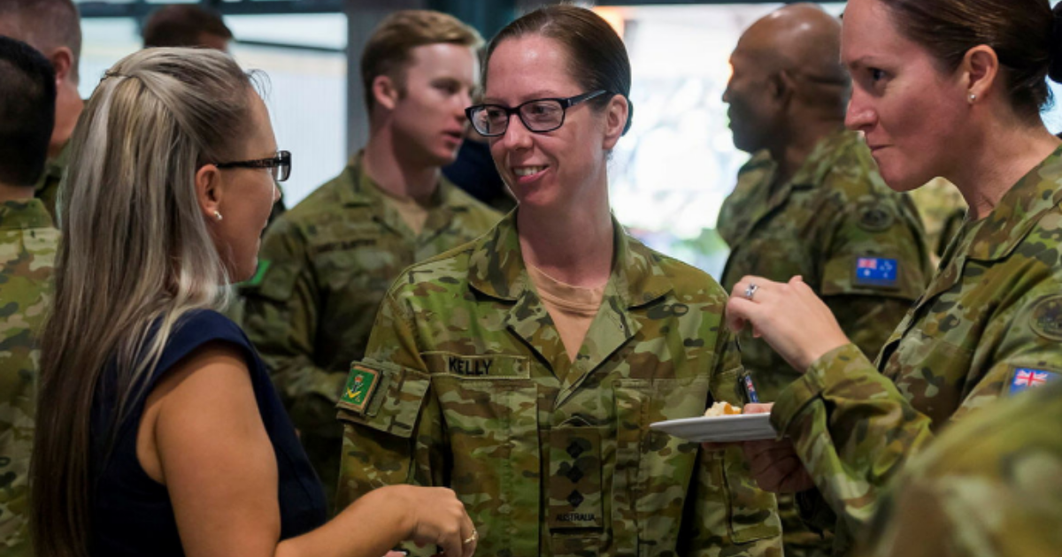 Two women in military uniforms and one in a black top talking.