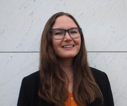 Photo of a young female with long brown hair and glasses and smiling